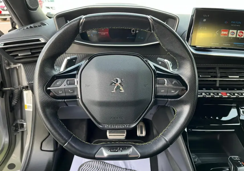 Volant GT en cuir perforé avec surpiqûres vertes du Peugeot 2008 II gris Artense, tableau de bord et écran tactile visibles.