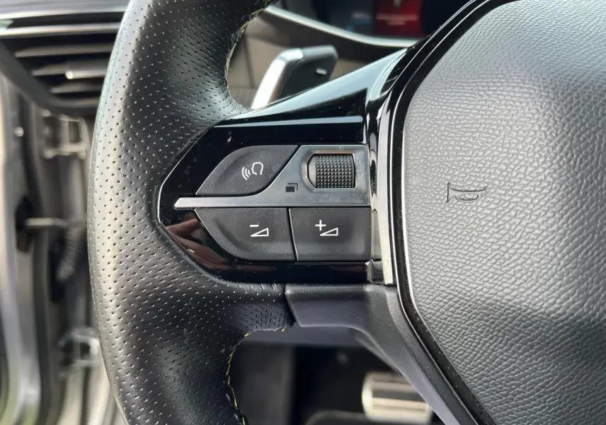 Gros plan sur les commandes gauche du volant en cuir perforé du Peugeot 2008 gris Artense toit noir de 2021.