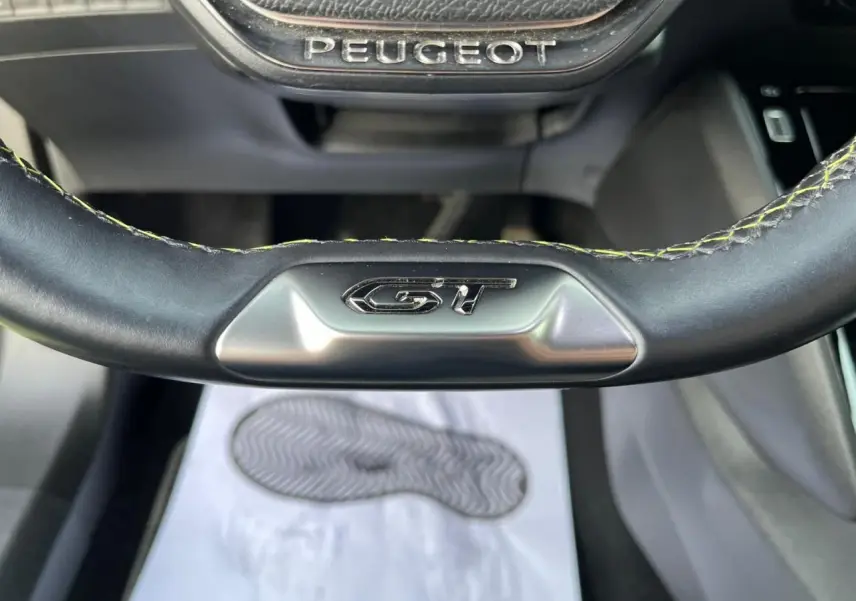 Gros plan sur le volant cuir noir avec surpiqûres vertes et logo GT du Peugeot 2008 II 1.2 PureTech 130.