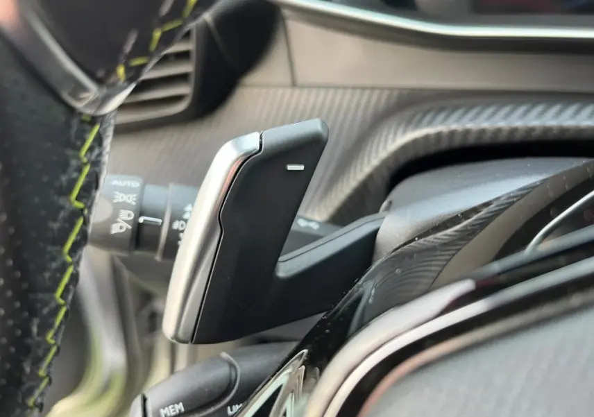 Gros plan sur la palette de changement de vitesses au volant d'un Peugeot 2008 gris Artense avec surpiqûres vertes.