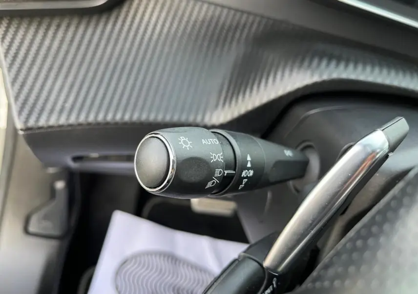 Gros plan sur la commande d'éclairage et le levier de régulateur du Peugeot 2008 gris avec intérieur noir texturé.