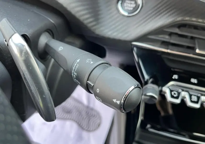 Gros plan sur la commande des essuie-glaces et le bouton start/stop dans l'habitacle du Peugeot 2008 gris avec toit noir.