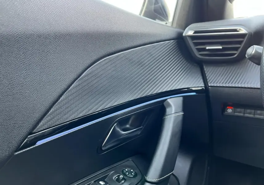 Détail intérieur côté gauche de la porte Peugeot 2008 gris Artense, avec garniture effet carbone et commandes de vitres.