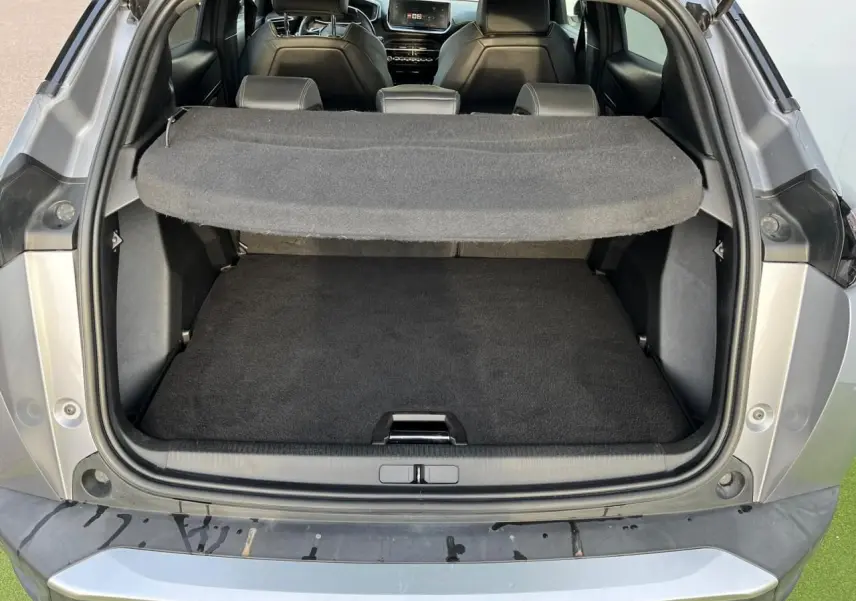 Coffre ouvert vu de l'arrière d'un Peugeot 2008 gris Artense avec intérieur noir et tablette cache-bagages déployée.
