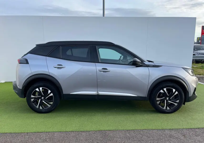 Profil droit d'un Peugeot 2008 gris Artense avec toit noir, jantes bi-tons 17'' et barres de toit noir brillant.