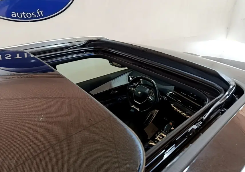 Vue plongeante sur l'intérieur noir du Peugeot 5008 bleu, mettant en valeur le volant et le tableau de bord moderne.