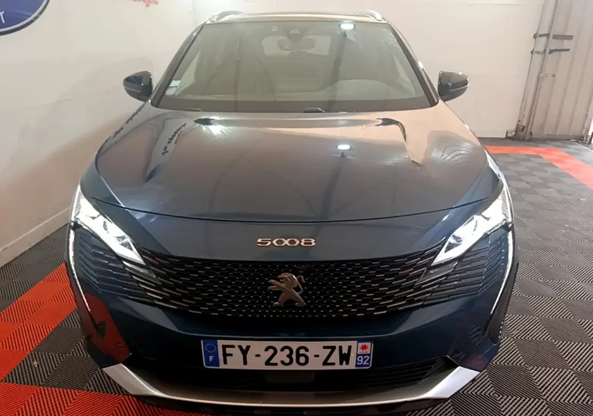 Vue frontale d'un Peugeot 5008 bleu 2021 avec calandre noire et phares LED allumés dans un garage.