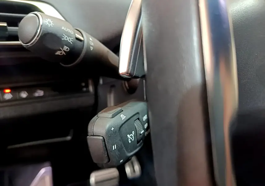 Gros plan sur les commandes au volant et levier d’éclairage du Peugeot 5008 GT 2021, intérieur noir.