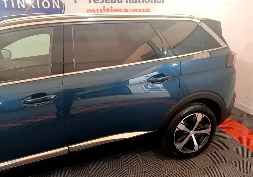 Vue latérale droite du Peugeot 5008 bleu avec jantes alliage et vitres teintées dans un showroom intérieur.