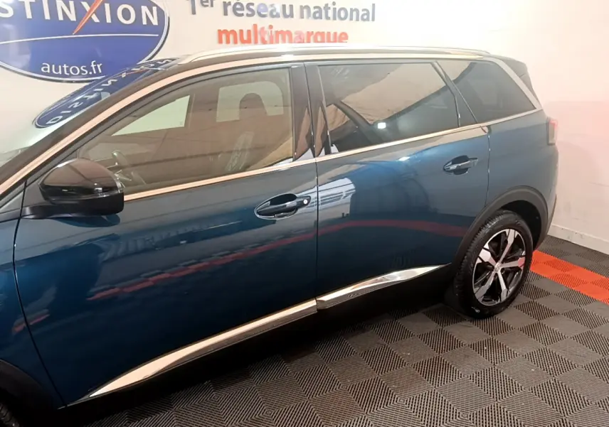 Profil côté gauche du Peugeot 5008 bleu 2021 avec jantes alliage et vitres teintées en intérieur showroom.
