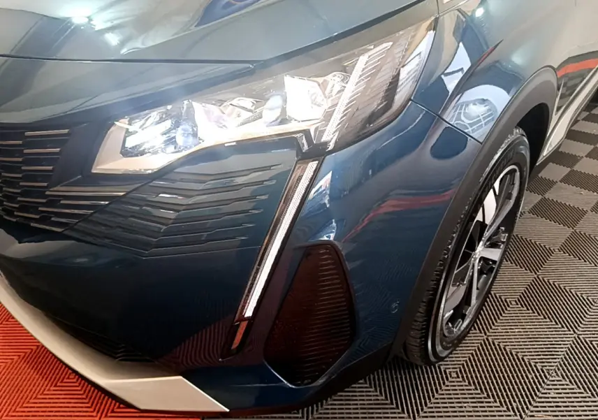 Gros plan sur l'avant droit bleu du Peugeot 5008 2021, mettant en valeur le phare LED et la calandre distinctive.