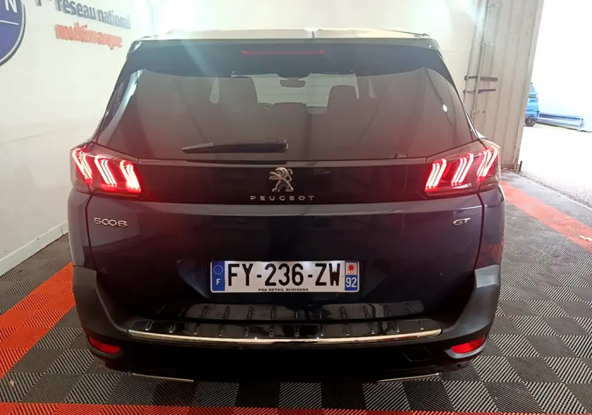 Vue arrière du Peugeot 5008 GT bleu avec feux LED caractéristiques allumés et plaque d'immatriculation française visible.