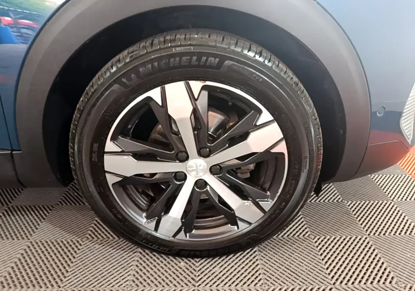 Gros plan sur la roue avant gauche du Peugeot 5008 bleu avec jante alliage bicolore et pneu Michelin.