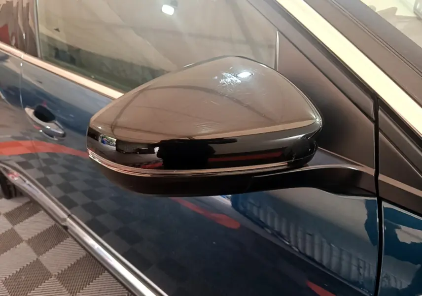 Rétroviseur noir côté gauche sur Peugeot 5008 bleu, vue rapprochée du miroir et porte avant.