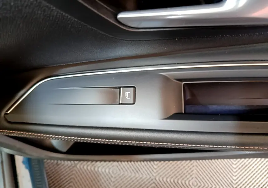 Gros plan sur la commande de lève-vitre en plastique noir mat, sur la porte intérieure côté conducteur du Peugeot 5008 bleu.