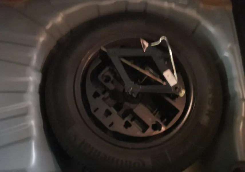 Gros plan sur la roue de secours en tôle noire dans le coffre d'une Renault Clio V gris schiste.