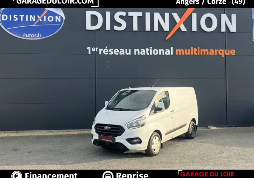 Vue 3/4 avant droite d'un Ford Transit Custom Fourgon blanc garé devant un mur gris avec logo Distinxion.