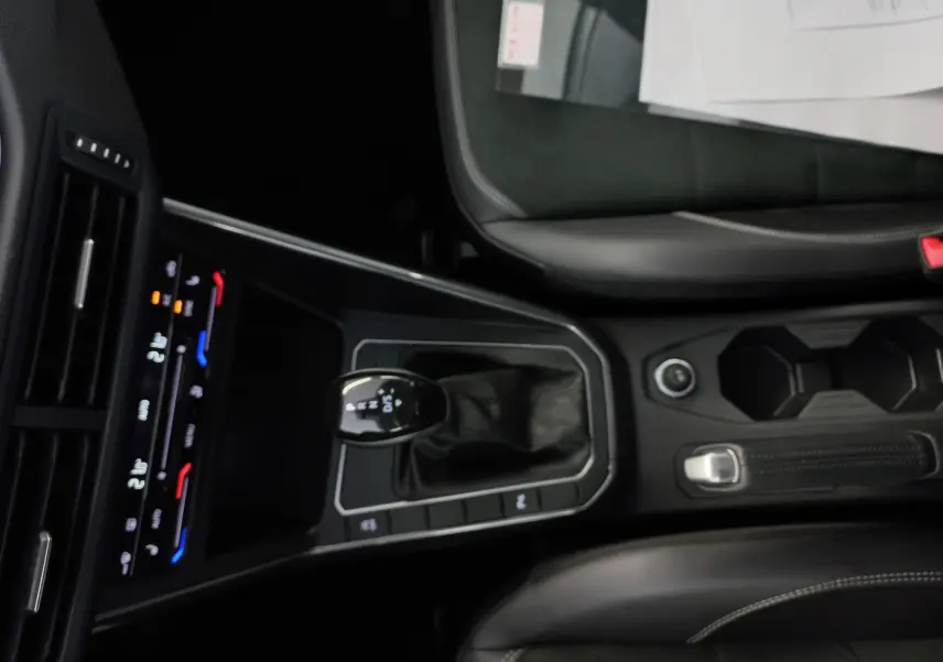 Vue intérieure centrée sur la console centrale d'une Volkswagen Polo 1.0 TSI 95 DSG7 avec levier de vitesse et sièges noirs.
