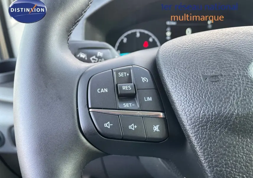Gros plan sur les commandes du volant noir du Ford Transit Fourgon blanc, mettant en valeur les boutons de régulateur et audio.