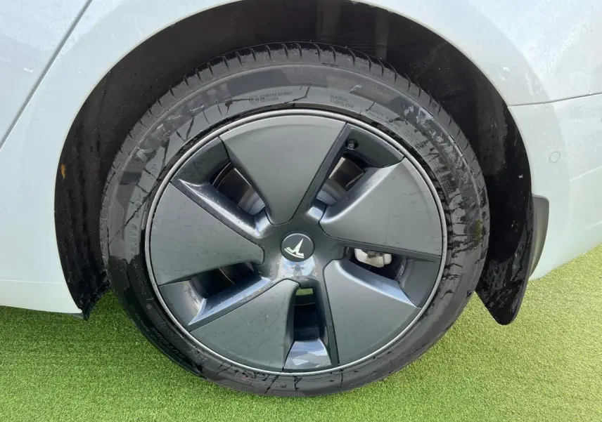 Gros plan sur la roue arrière droite d'une Tesla Model 3 blanche avec jante aérodynamique grise.