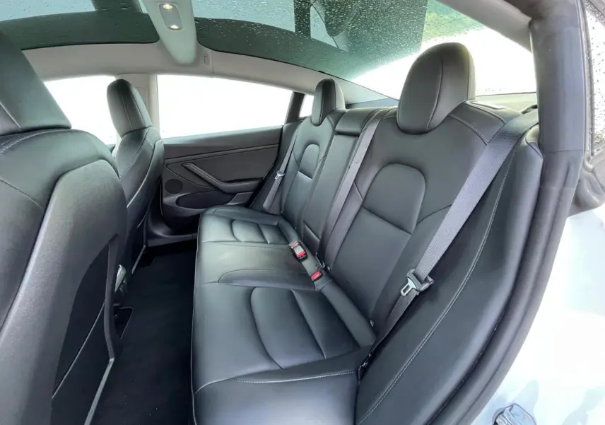 Vue intérieure arrière droite de la Tesla Model 3 Standard Plus blanche, sièges en cuir noir et toit panoramique en verre.