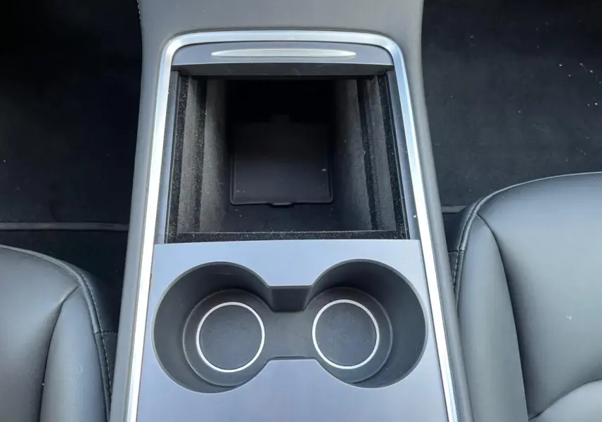 Vue plongeante sur la console centrale noire avec porte-gobelets et rangement entre les sièges avant en cuir noir.