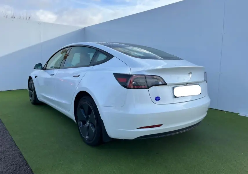 Tesla Model 3 blanc vue 3/4 arrière côté gauche, avec jantes noires et toit panoramique en verre visible.