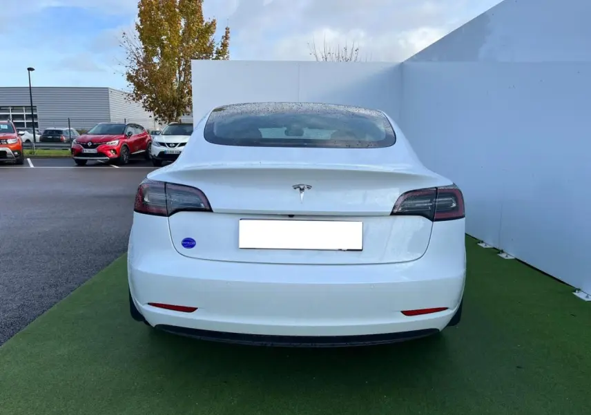 Vue arrière d'une Tesla Model 3 blanche 2022 avec feux arrière sombres et pare-chocs ton caisse.