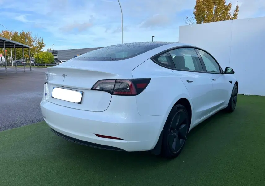 Vue 3/4 arrière droite d'une Tesla Model 3 blanche 2022 avec jantes noires et toit panoramique en verre.