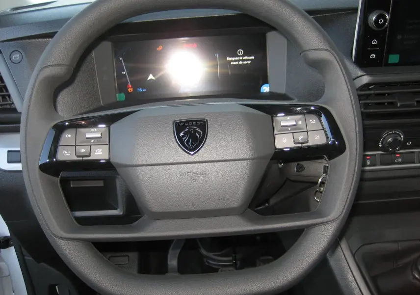 Vue rapprochée du volant gris foncé du Peugeot Expert Fourgon 2025 avec commandes intégrées et écran digital en arrière-plan.