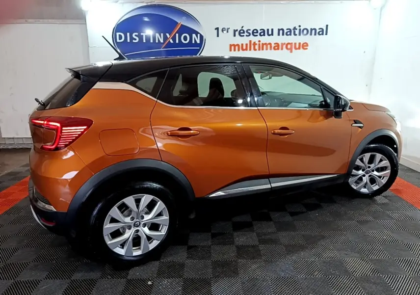 Vue de profil côté droit d'un Renault Captur jaune orangé 2020 dans un showroom avec jantes alliage et feux arrière LED allumés.