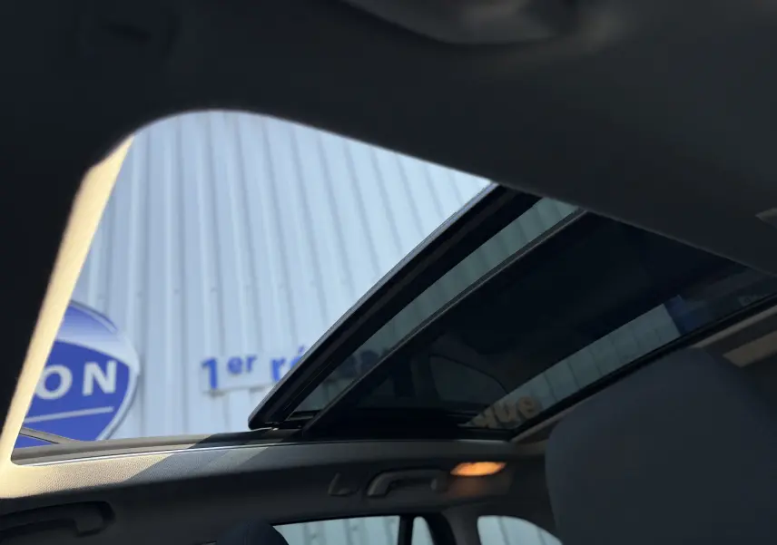 Toit ouvrant panoramique ouvert sur l'intérieur d'un BMW X1 blanc, vue depuis les sièges arrière vers le ciel.