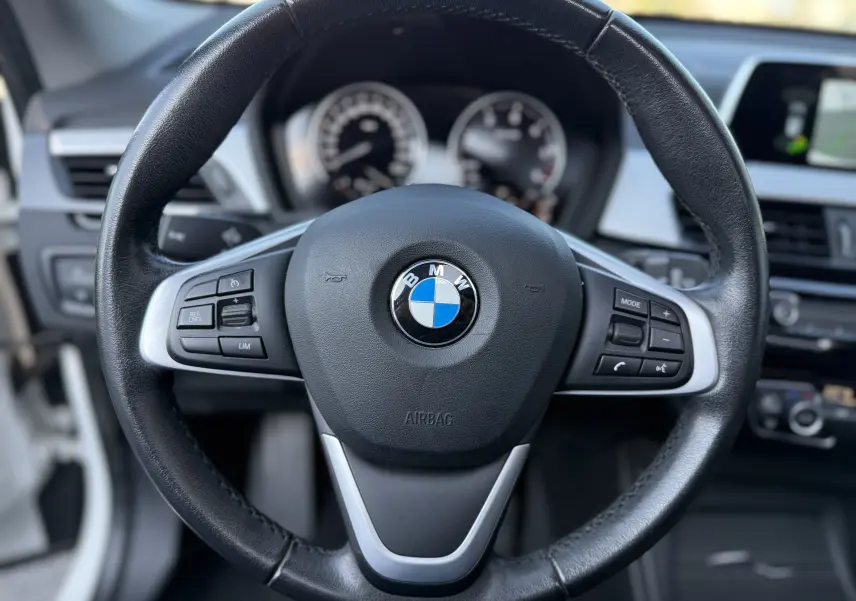 Gros plan sur le volant en cuir noir de la BMW X1 20D 2018, avec commandes intégrées et tableau de bord flou en arrière-plan.