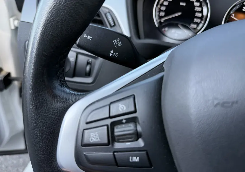 Gros plan sur le volant côté gauche d’un BMW X1 blanc, avec commandes de régulateur de vitesse visibles.
