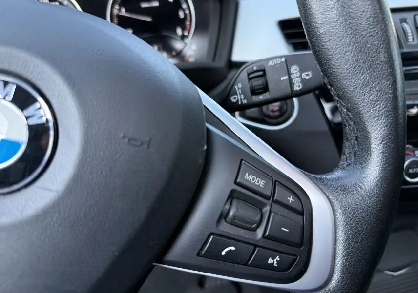 Gros plan sur le volant cuir noir côté droit du BMW X1 blanc 2018, avec commandes multimédia intégrées.