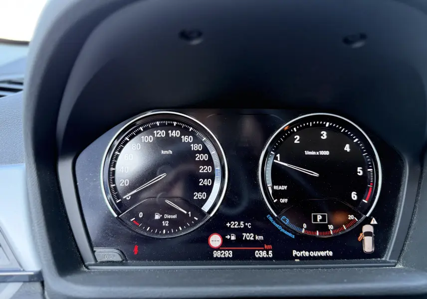 Tableau de bord du BMW X1 20D 2018 montrant la vitesse, le compte-tours, et l'affichage digital avec porte ouverte.