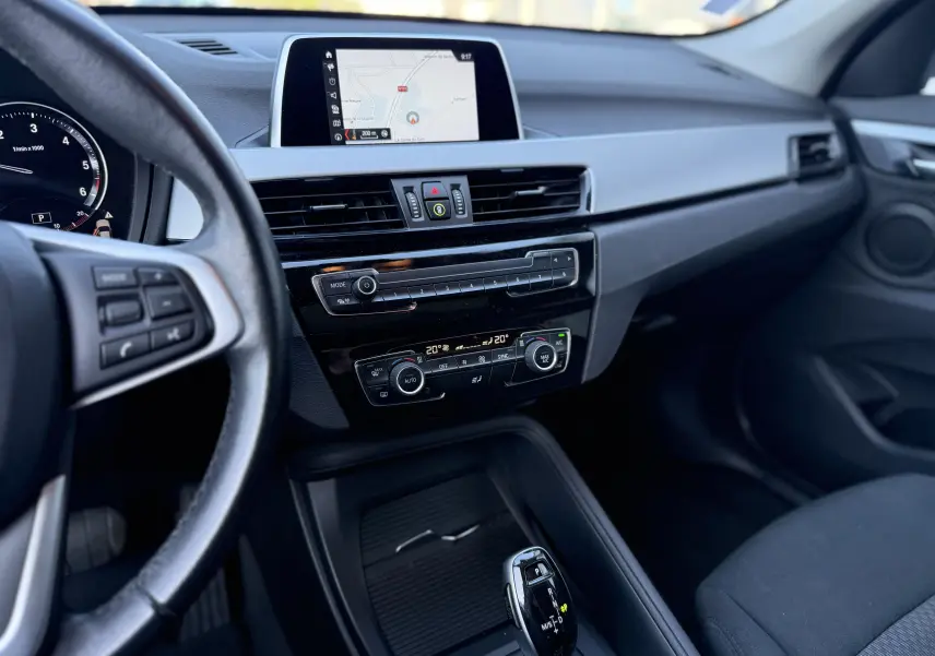 Vue intérieure côté conducteur du tableau de bord du BMW X1 blanc 2018 avec écran GPS et commandes climatisation.
