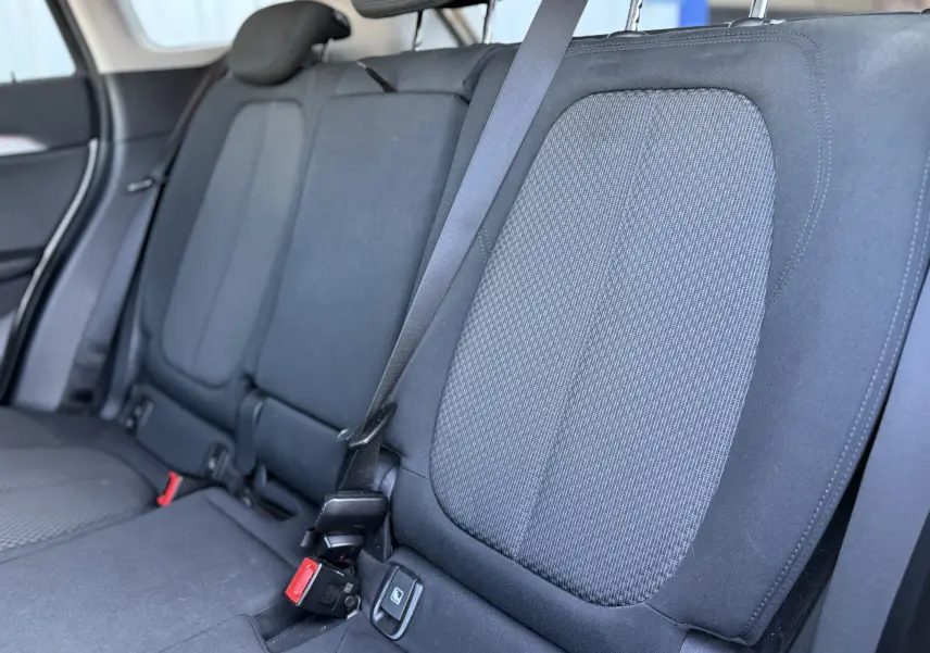 Vue rapprochée des sièges arrière en tissu noir du BMW X1 20D blanc, montrant les ceintures de sécurité et appuie-têtes.