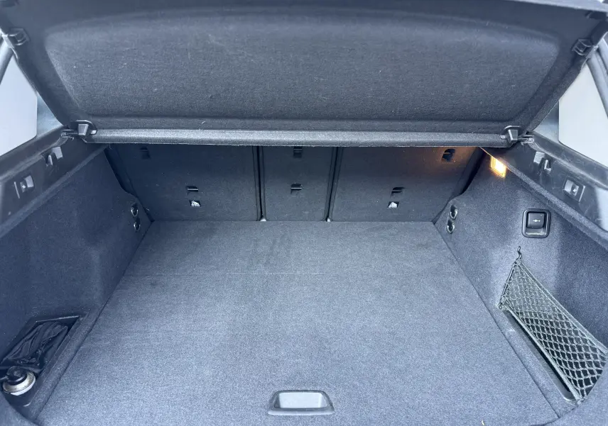 Coffre ouvert vu de l'arrière d'un BMW X1 blanc, montrant un espace de chargement propre et bien agencé avec filet latéral.