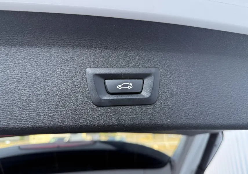 Bouton de fermeture électrique du hayon sur la partie intérieure d’un BMW X1 blanc, vue rapprochée.