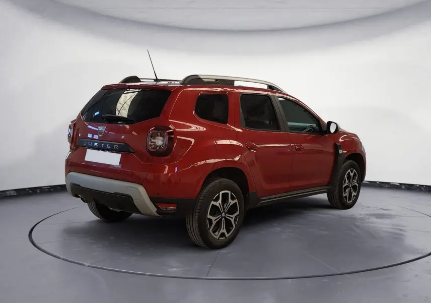 Dacia Duster rouge fusion en 3/4 arrière droit, avec barres de toit noires et jantes alliage 17 pouces.