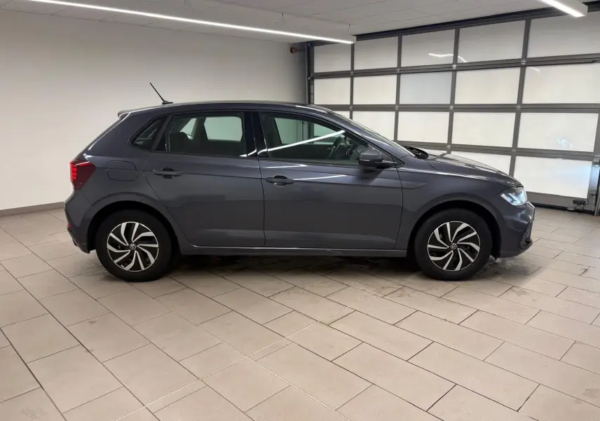 Vue de profil côté gauche d'une Volkswagen Polo gris cendre 2024 dans un garage lumineux avec jantes au design moderne.