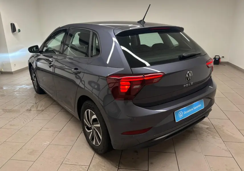 Volkswagen Polo gris cendre vue 3/4 arrière droit dans un showroom avec feux arrière allumés.