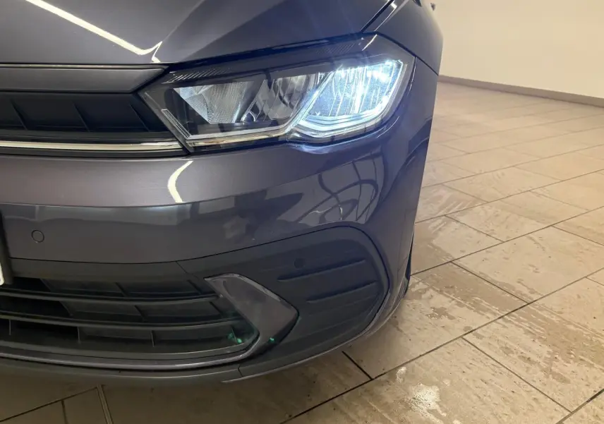 Gros plan sur le phare avant droit allumé d'une Volkswagen Polo gris cendre 2024 dans un intérieur lumineux.