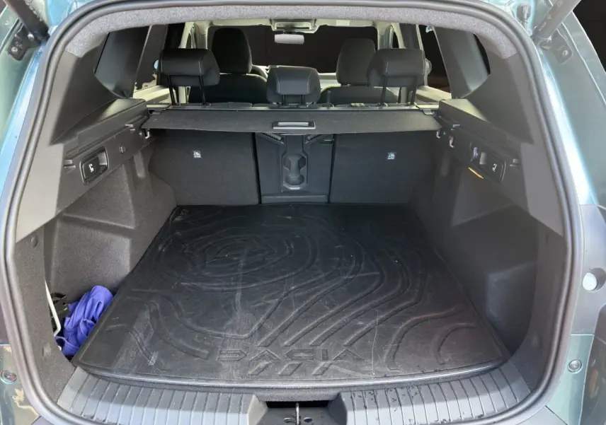 Vue arrière du coffre ouvert d'un Dacia Bigster vert, montrant la grande capacité et la protection de tapis noir marqué Dacia.