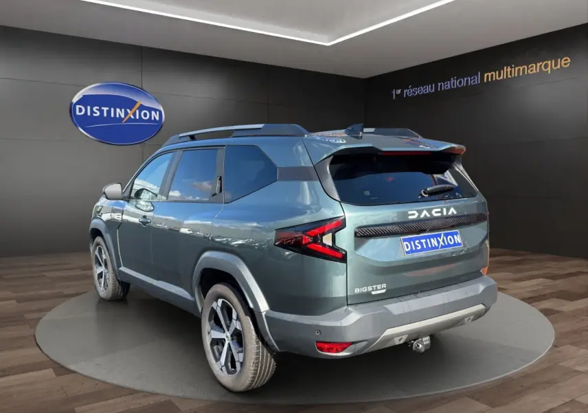 Vue 3/4 arrière droite du Dacia Bigster vert avec attelage RDSO, feux LED et jantes alliage visibles en showroom.