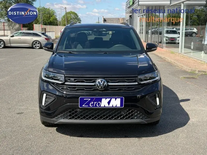 Vue avant d'un Volkswagen T-Cross noir avec calandre chromée et feux LED, stationné devant un bâtiment vitré.