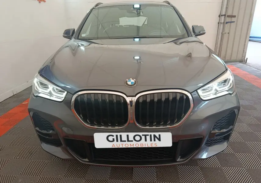 Vue frontale d'un BMW X1 sDrive18i M Sport gris métallisé avec phares LED allumés dans un garage.