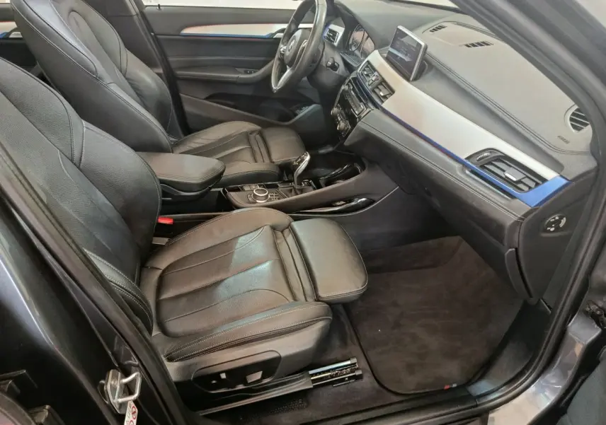 Intérieur BMW X1 sDrive18i M Sport 2019 vu côté conducteur, sièges cuir noirs et tableau de bord avec écran tactile.