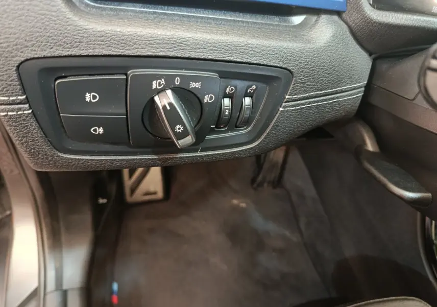 Gros plan sur le panneau de commande des phares à gauche du volant dans l'habitacle noir du BMW X1 sDrive18i M Sport 2019.